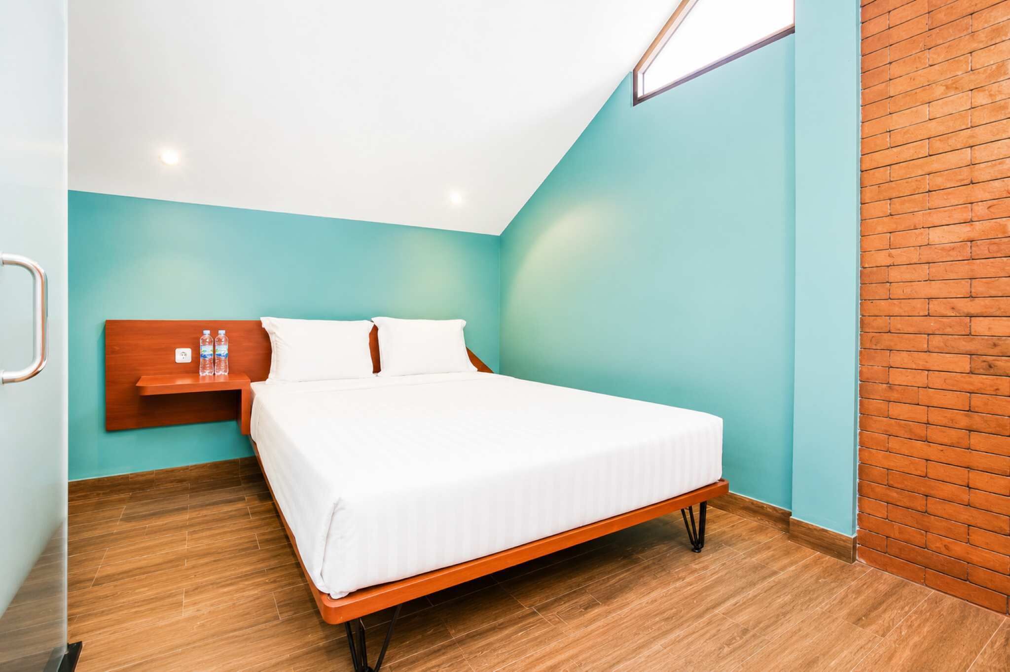 A single bed with a wooden headboard, a nightstand with water bottles, and a light fixture above the bed.