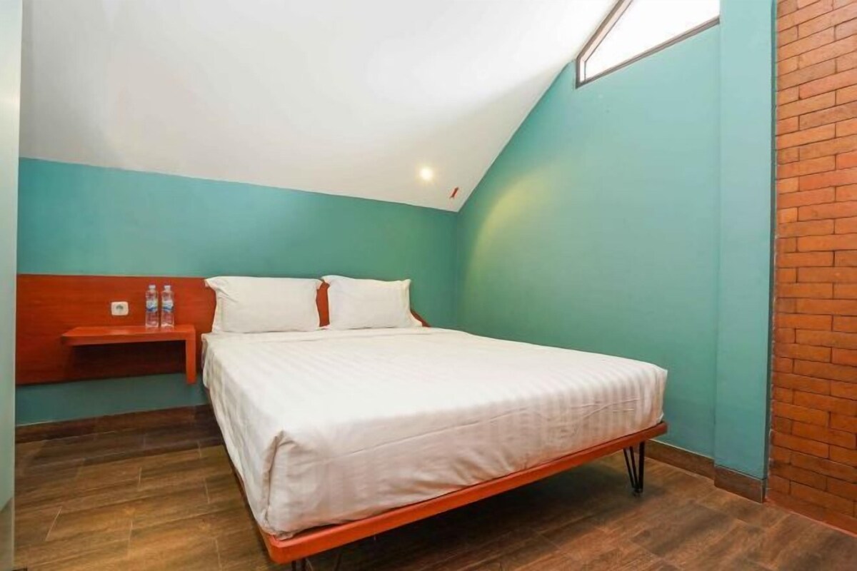A single bed with a wooden frame, white bedding, and a small bedside table with bottles.