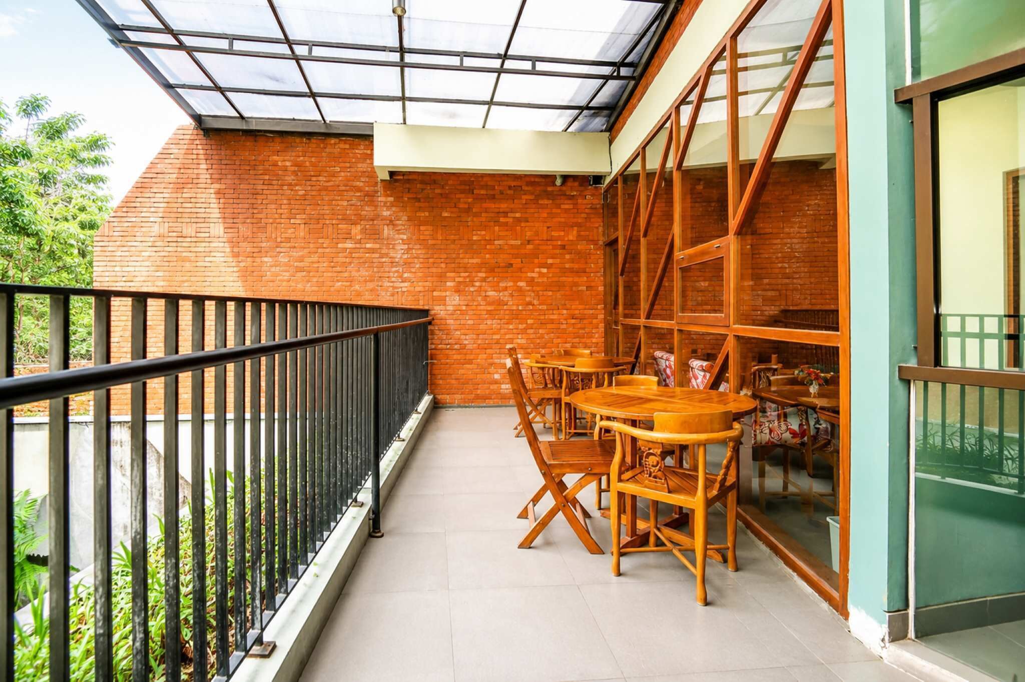 Un balcón con barandilla de vidrio, pared de ladrillo y mesa de madera con sillas.