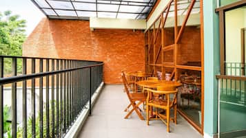 Un balcón con barandilla de vidrio, pared de ladrillo y mesa de madera con sillas.