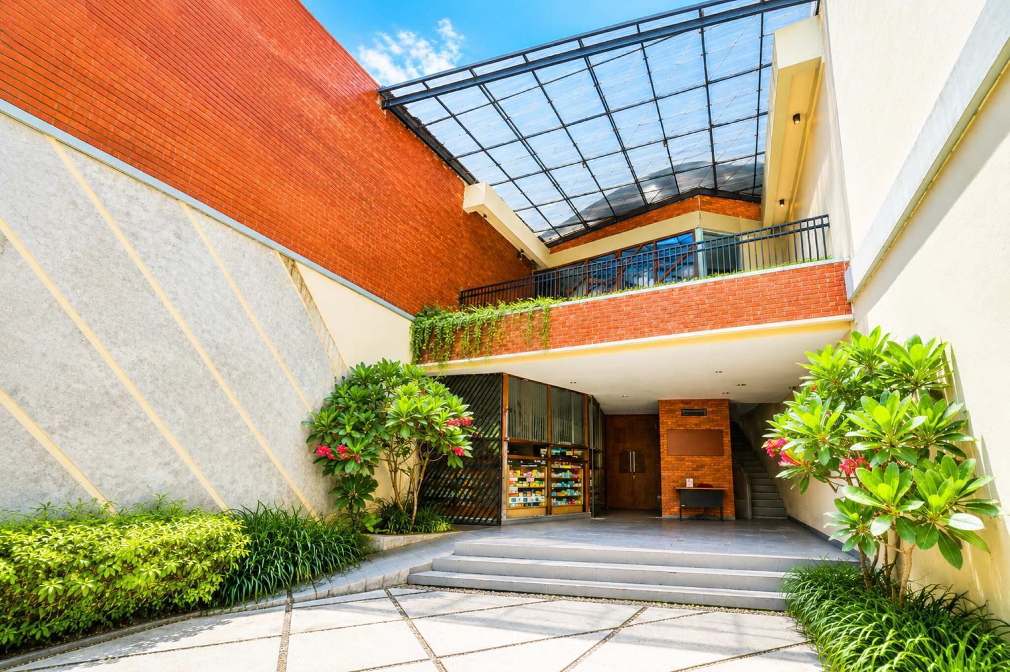 A modern building with a glass roof, brick walls, and a central staircase leading to a second-floor balcony.