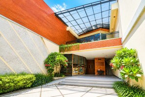 Ein modernes Gebäude mit Glasdach, Backsteinwänden und einer zentralen Treppe, die zu einem Balkon im zweiten Stock führt.