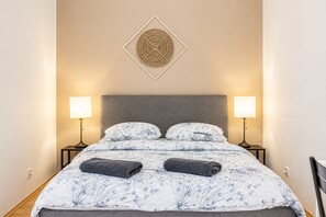 Ein ordentlich bezogenes Bett mit einem blumigen Überwurf, zwei Nachttischlampen und einem Wanddekor.