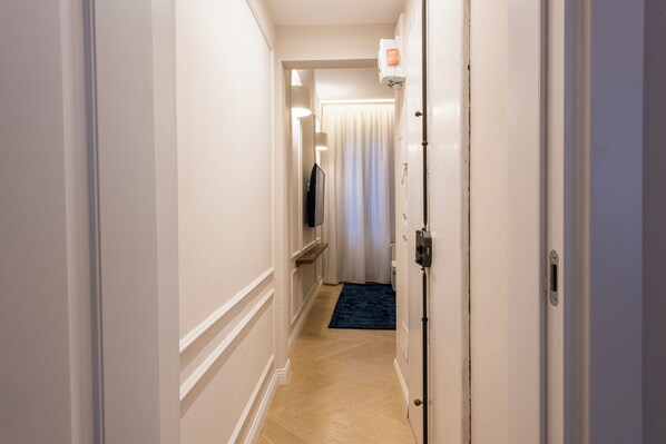 Un pasillo de hotel con suelo de madera, paredes blancas, alfombra azul y una puerta con interruptor de luz.