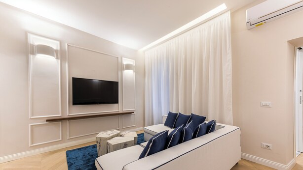 A modern living room with a white sofa, a flat-screen TV mounted on the wall, a small coffee table, and a blue rug. - Blue Santa Croce by MMega (Florence)