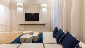 A modern living room with a flat-screen TV mounted on the wall, a sofa with blue cushions, marble side tables, and a blue carpet. - Blue Santa Croce by MMega (Florence)