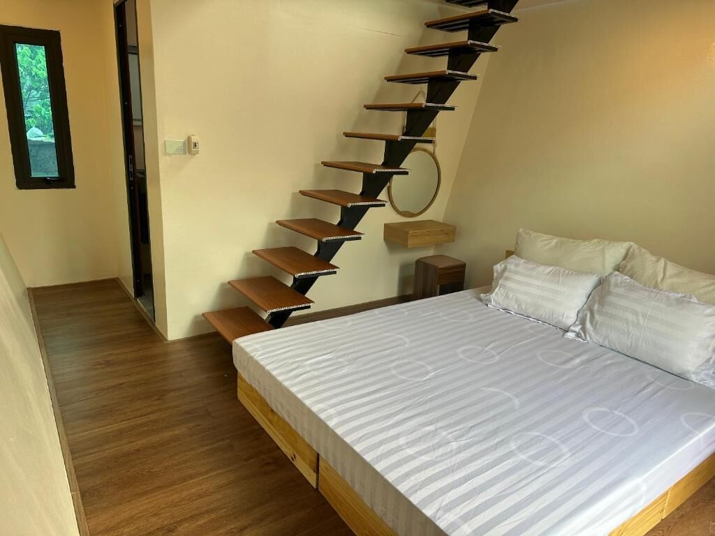 A bedroom with a wooden bed, a white mattress, a wooden staircase, and a small bedside table.