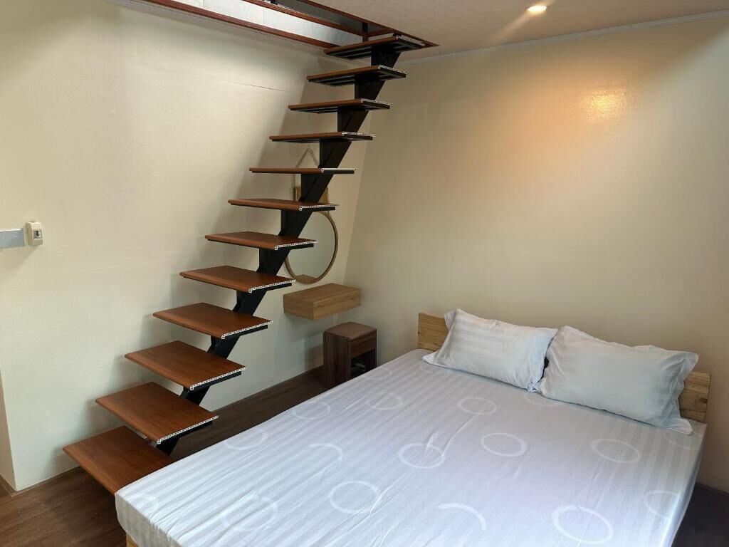 A bedroom with a bed, a white mattress, a wooden headboard, a white pillow, a wooden nightstand, and a spiral staircase.