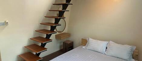 A bedroom with a bed, a white mattress, a wooden headboard, a white pillow, a wooden nightstand, and a spiral staircase.