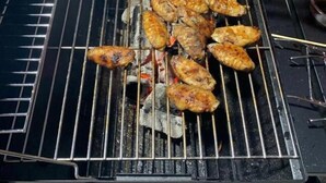 Un barbecue avec des ailes de poulet et des saucisses en train de cuire.