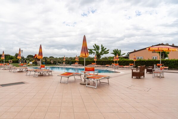 A poolside area with sun loungers and umbrellas, a swimming pool, and a building in the background.