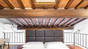 A bedroom with a wooden ceiling, a dark headboard, a wooden nightstand, and a metal railing. - Hotiday Apartments Costa degli Etruschi (Rosignano Marittimo)