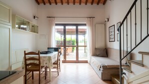 A room with a dining table, chairs, a sofa, a staircase, and a sliding glass door leading to an outdoor area. - Hotiday Apartments Costa degli Etruschi (Rosignano Marittimo)