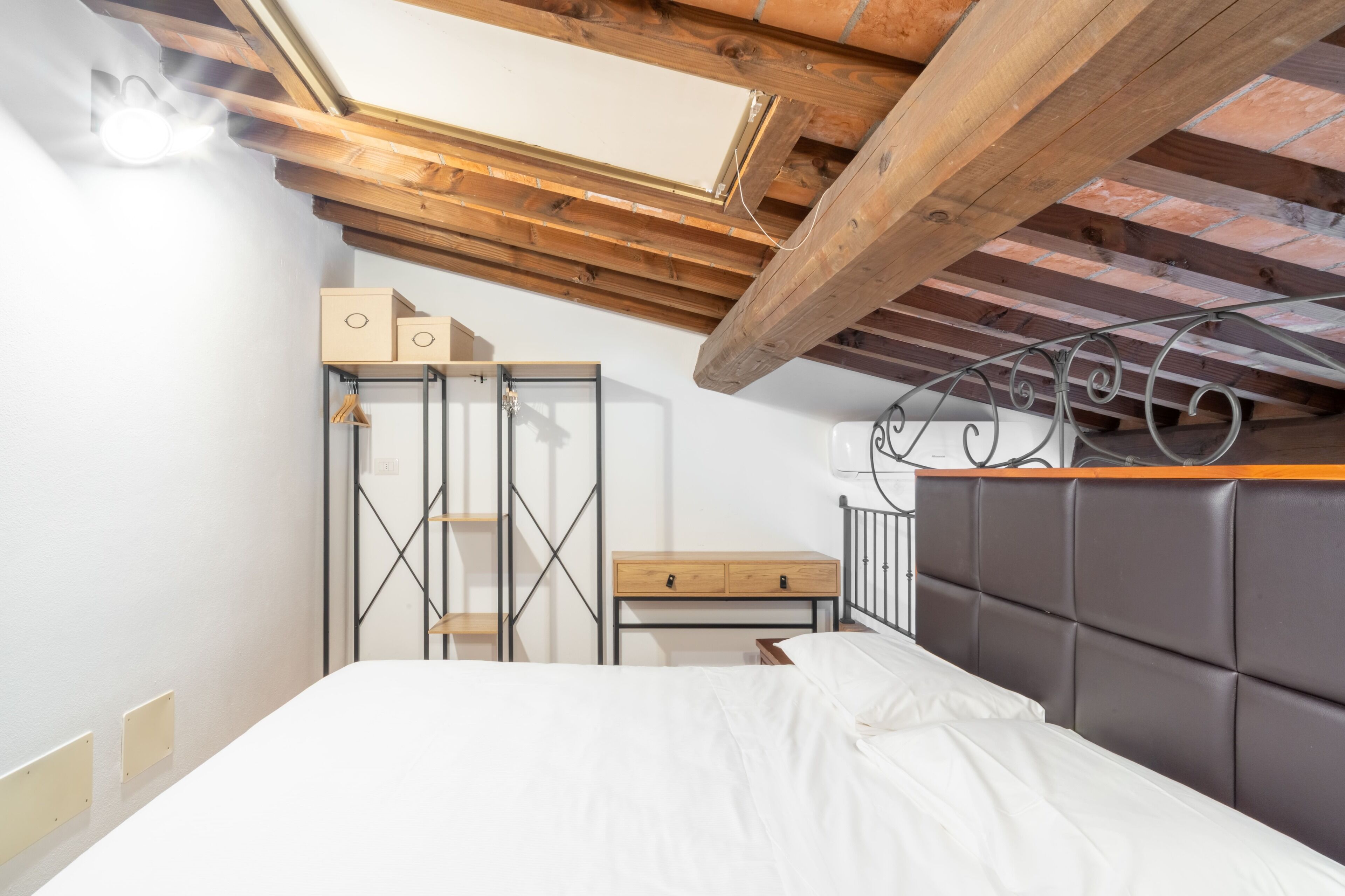 A bedroom with a bed, a nightstand, a dresser, and a skylight.