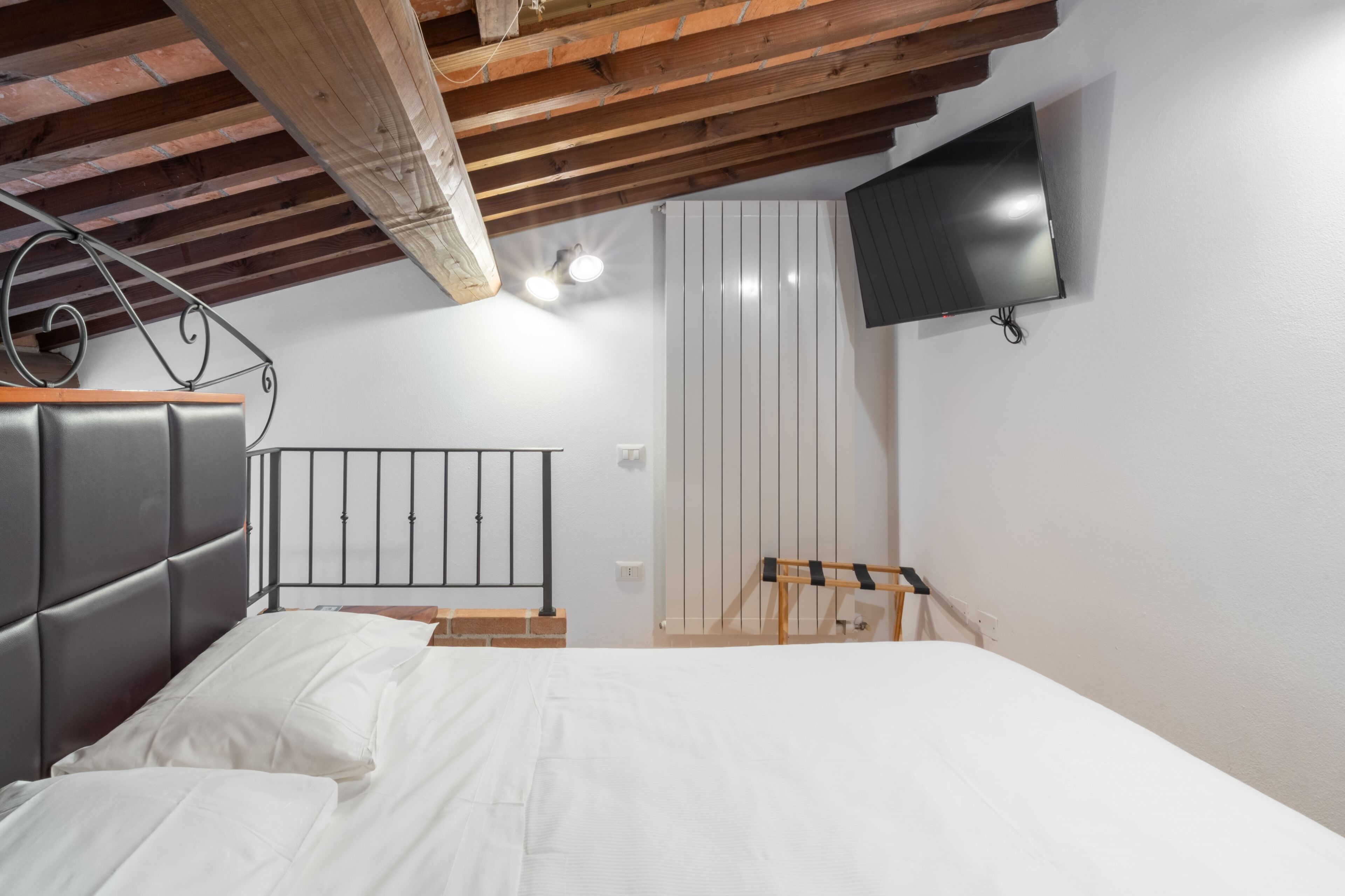 Une chambre à coucher avec un lit, un téléviseur fixé au mur et un plafond en bois.
