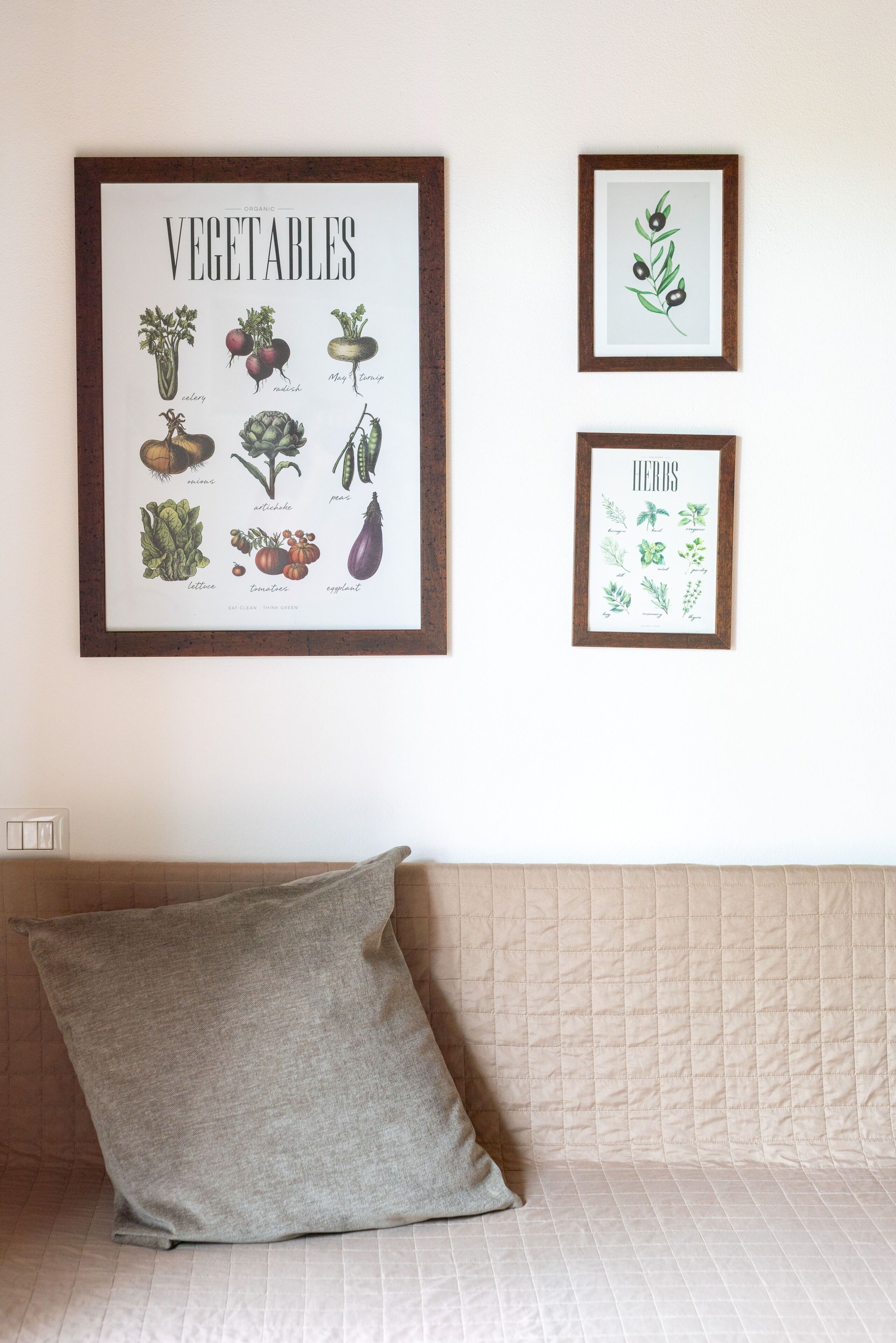 A framed vegetable and herb illustration on a wall, a quilted sofa, and a grey pillow.