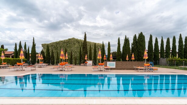 A swimming pool with lounge chairs and umbrellas, surrounded by trees and a hedge. - Hotiday Apartments Costa degli Etruschi (Rosignano Marittimo)