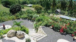 A lush garden with a paved pathway, large rocks, and a small house in the background. - Panorama de Argao Boutique Resort (Argao)
