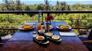 A dining table set with plates, bowls, and glasses, overlooking a tropical landscape with palm trees and the ocean. - Panorama de Argao Boutique Resort (Argao)
