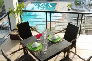 A table set for two with green plates, a glass, and a vase with red flowers on a balcony overlooking a pool. - Panorama de Argao Boutique Resort (Argao)