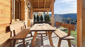 A wooden deck with a table and benches, overlooking a forested landscape. - Chalet Hugo with Mountain Views, Shared Pool, and Wi-Fi (Vöran)