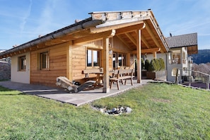 A wooden cabin with a covered patio, a stone pathway, and a small garden area. - Chalet 'Hugo' with Mountain View, Shared Pool and Wi-Fi (Vöran)