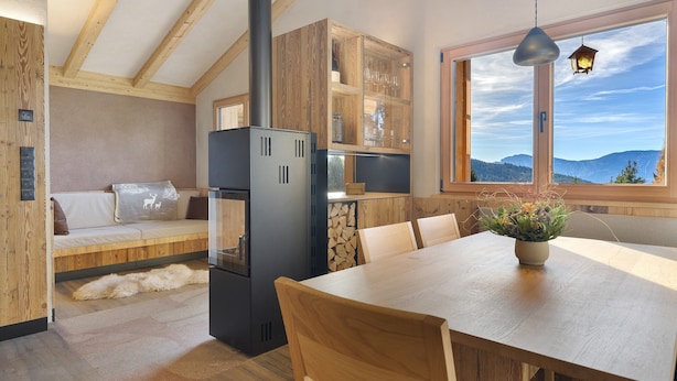 A modern kitchen with a large window, wooden beams, a dining table, and a built-in stove. - Chalet Hugo with Mountain Views, Shared Pool, and Wi-Fi (Vöran)