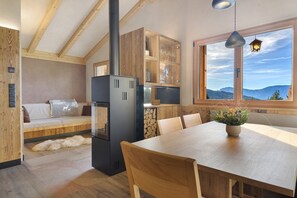 A modern kitchen with a large window, wooden beams, a dining table, and a built-in stove. - Chalet Hugo with Mountain Views, Shared Pool, and Wi-Fi (Vöran)