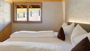 A bedroom with a wooden ceiling, a large window with a view of a stone wall and a wooden fence, and a bed with white and brown bedding. - Chalet Hugo with Mountain Views, Shared Pool, and Wi-Fi (Vöran)