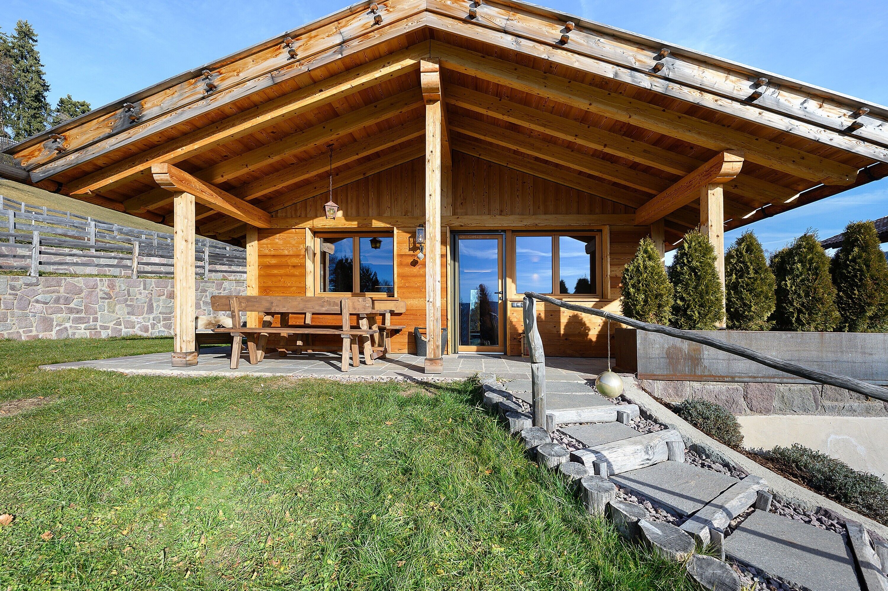 Eine Holzhütte mit überdachter Veranda, Steinmauern und einer Steintreppe, die zum Eingang führt.