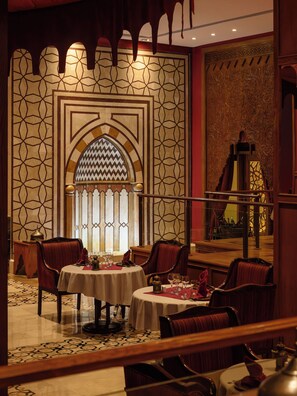 A dining area with a patterned wall, a large arched window, and a view of a pool. - The Makadi Spa Hotel Couples 18 plus (Makadi Bay)
