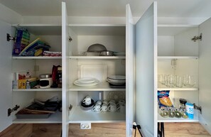 Une cuisine avec des placards ouverts contenant de la vaisselle, des ustensiles de cuisine et des en-cas.