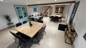 A spacious dining area with a large wooden table and multiple chairs, surrounded by large windows offering views of greenery. - Group Gîte: Domaine de la Vacquerie (Alette)