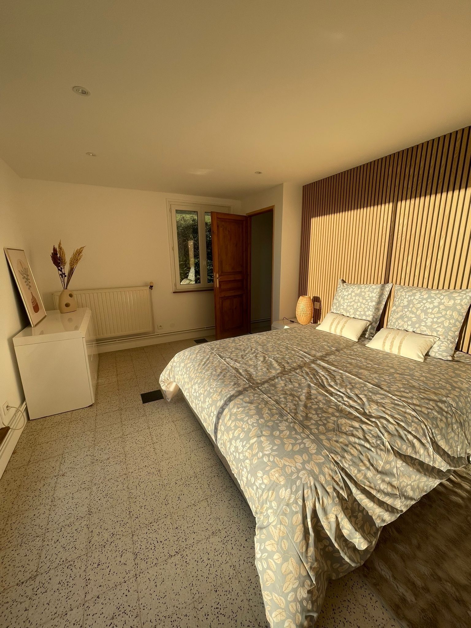 A bedroom with a bed, a bedside table, a window, and a radiator.
