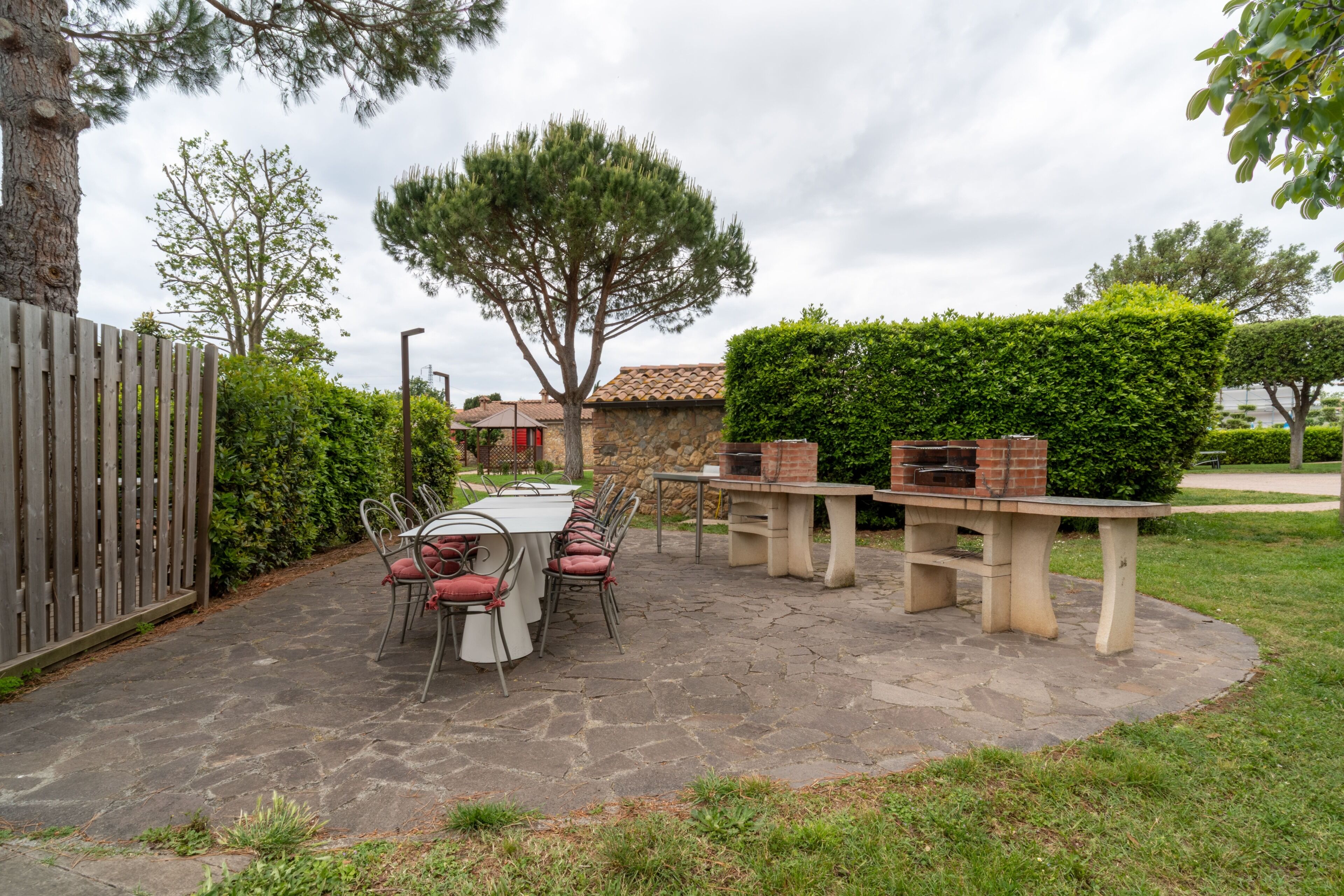 An outdoor patio with a stone table and chairs, surrounded by greenery and a wooden fence.