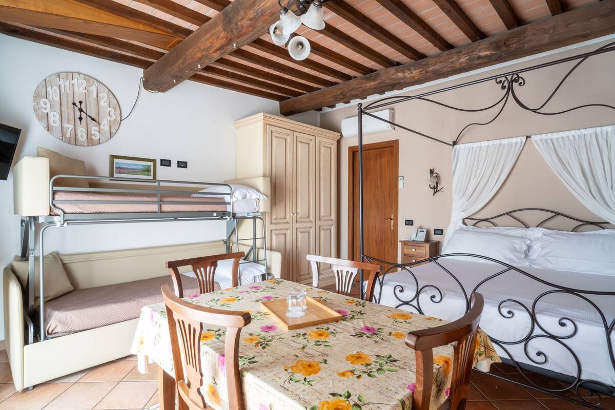 A room with bunk beds, a dining table, chairs, a clock, a wardrobe, and a bed with a canopy.