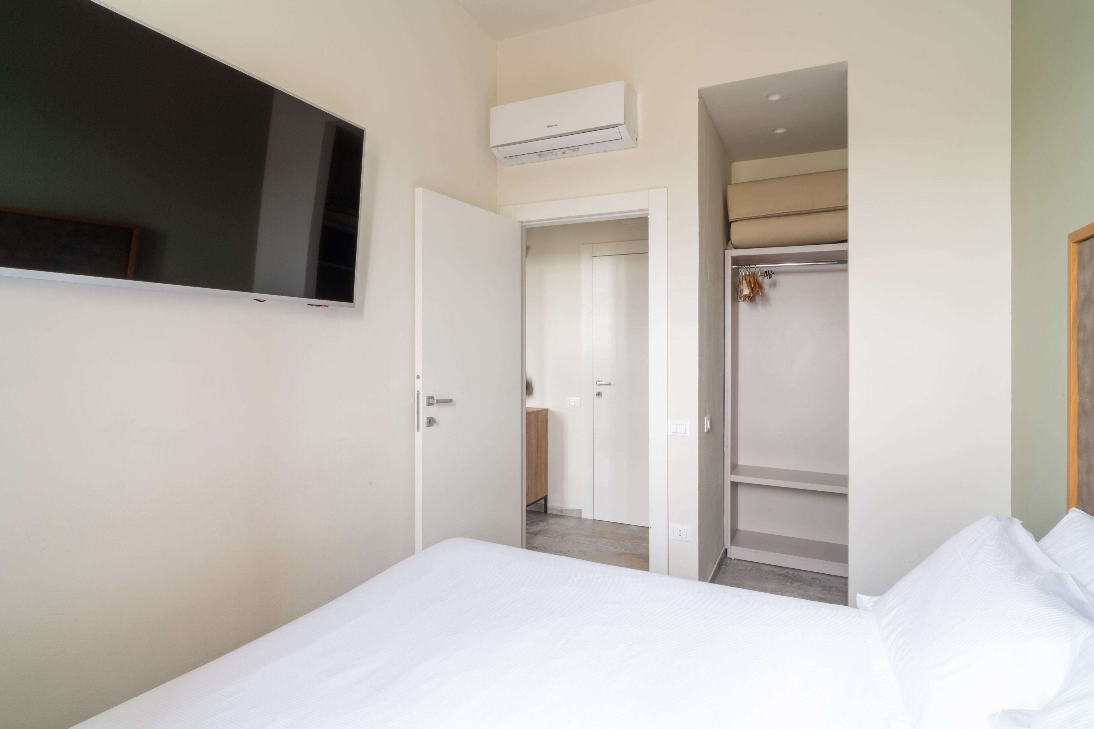 A bedroom with a bed, a TV mounted on the wall, a closet, and an air conditioning unit.
