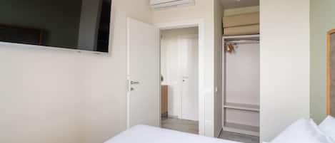 Ein Schlafzimmer mit Bett, Wand-Fernseher, Kleiderschrank und Klimaanlage.