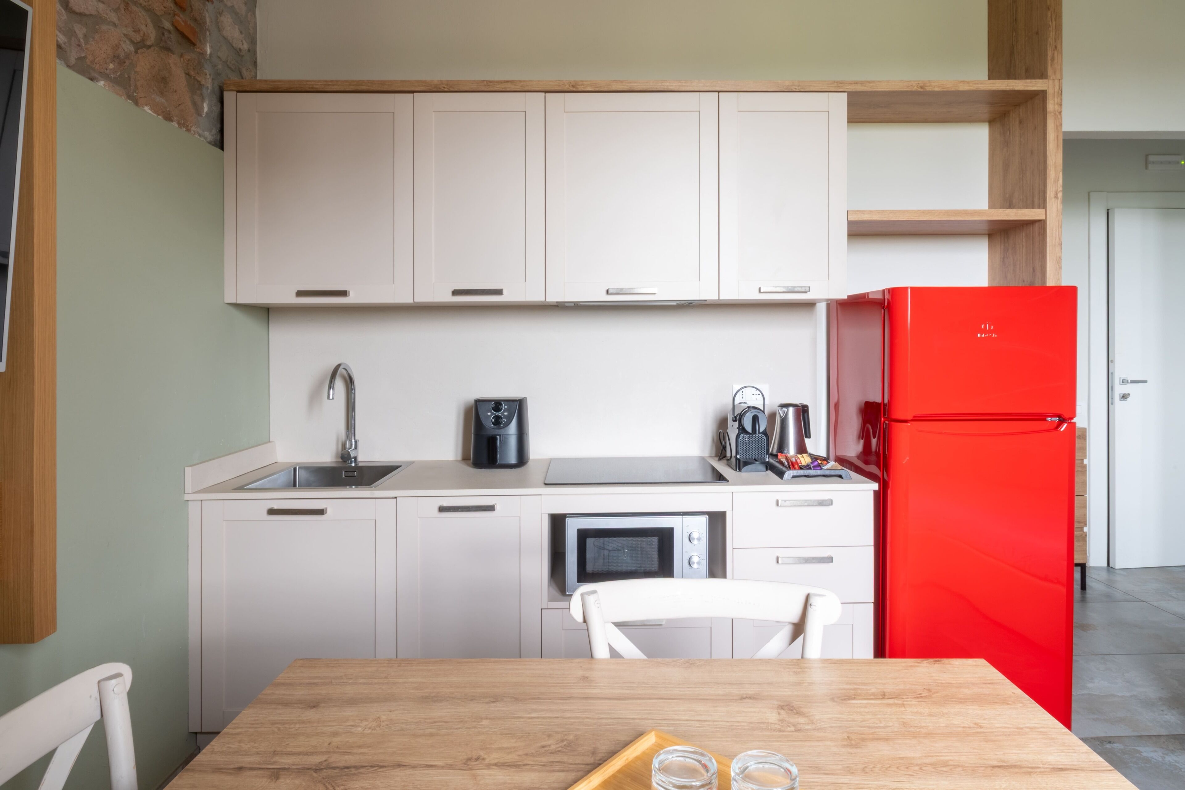 Una cocina con armarios blancos, un refrigerador rojo, un microondas y una cafetera.