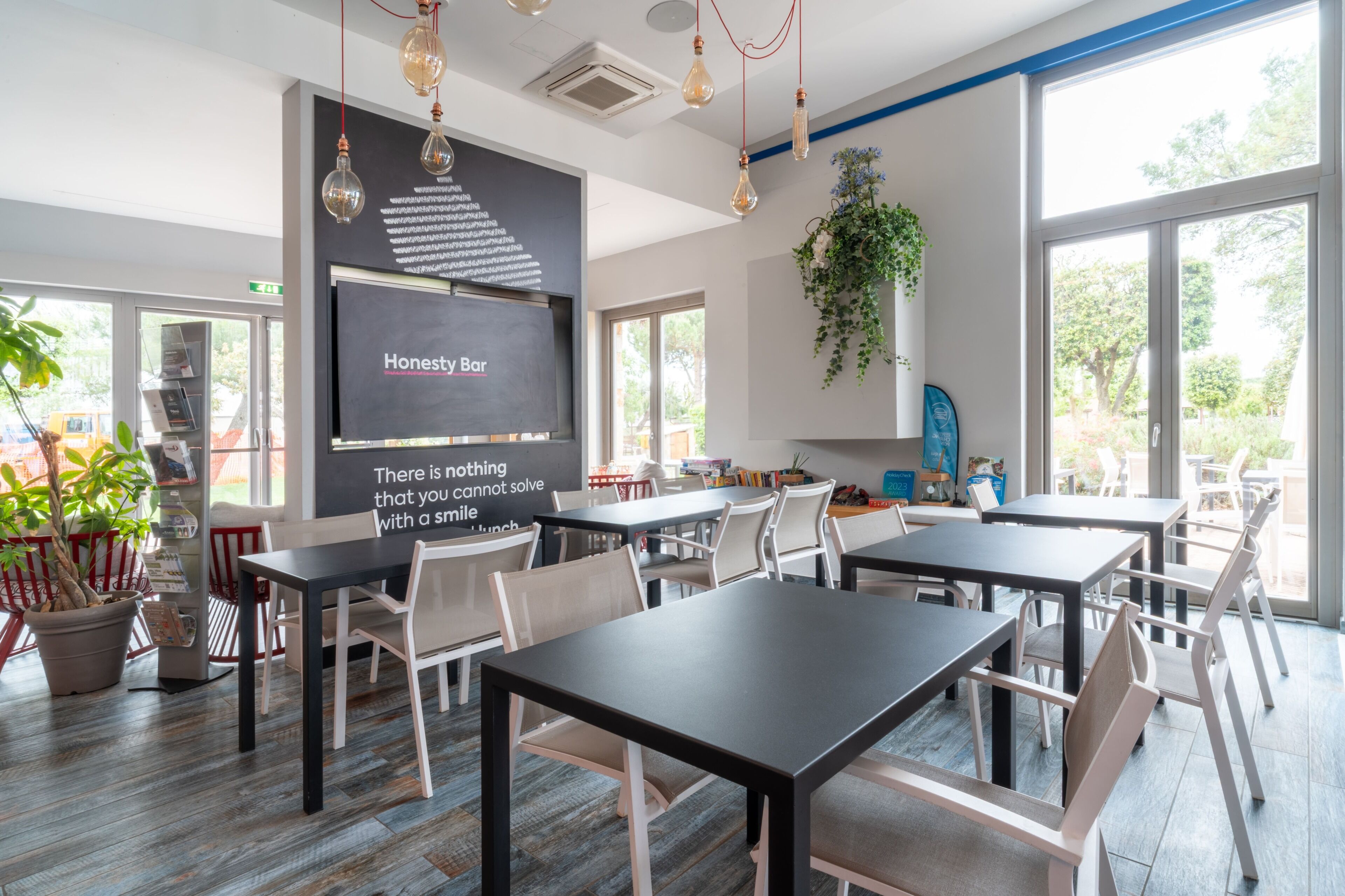Ein modernes Restaurant mit Tischen, Stühlen und einer Tafel mit Schrift, ausgestattet mit großen Fenstern.