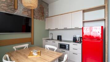Una cocina moderna con armarios blancos, un refrigerador rojo, un microondas y un comedor con mesa de madera y sillas blancas.