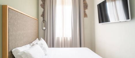 Ein Hotelzimmer mit Bett, Wandfernseher und einem Vorhangfenster.
