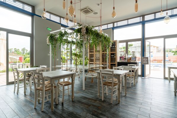 Un restaurante con mesas y sillas blancas, un arreglo floral central y grandes ventanales.