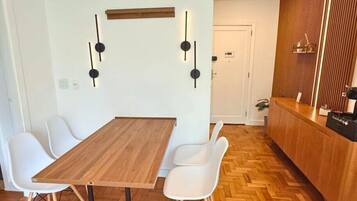 Uma sala de jantar moderna com mesa de madeira e cadeiras brancas, piso de madeira em padrão herringbone e parede de madeira com prateleira embutida.