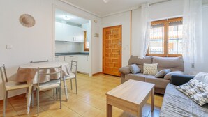 A living room with a sofa, a dining table with chairs, a wooden door, and a window with curtains. - Bungalow 'Fontilles 3 En Santa Pola' with Private Terrace, Wi-Fi and Air Conditioning (Santa Pola)