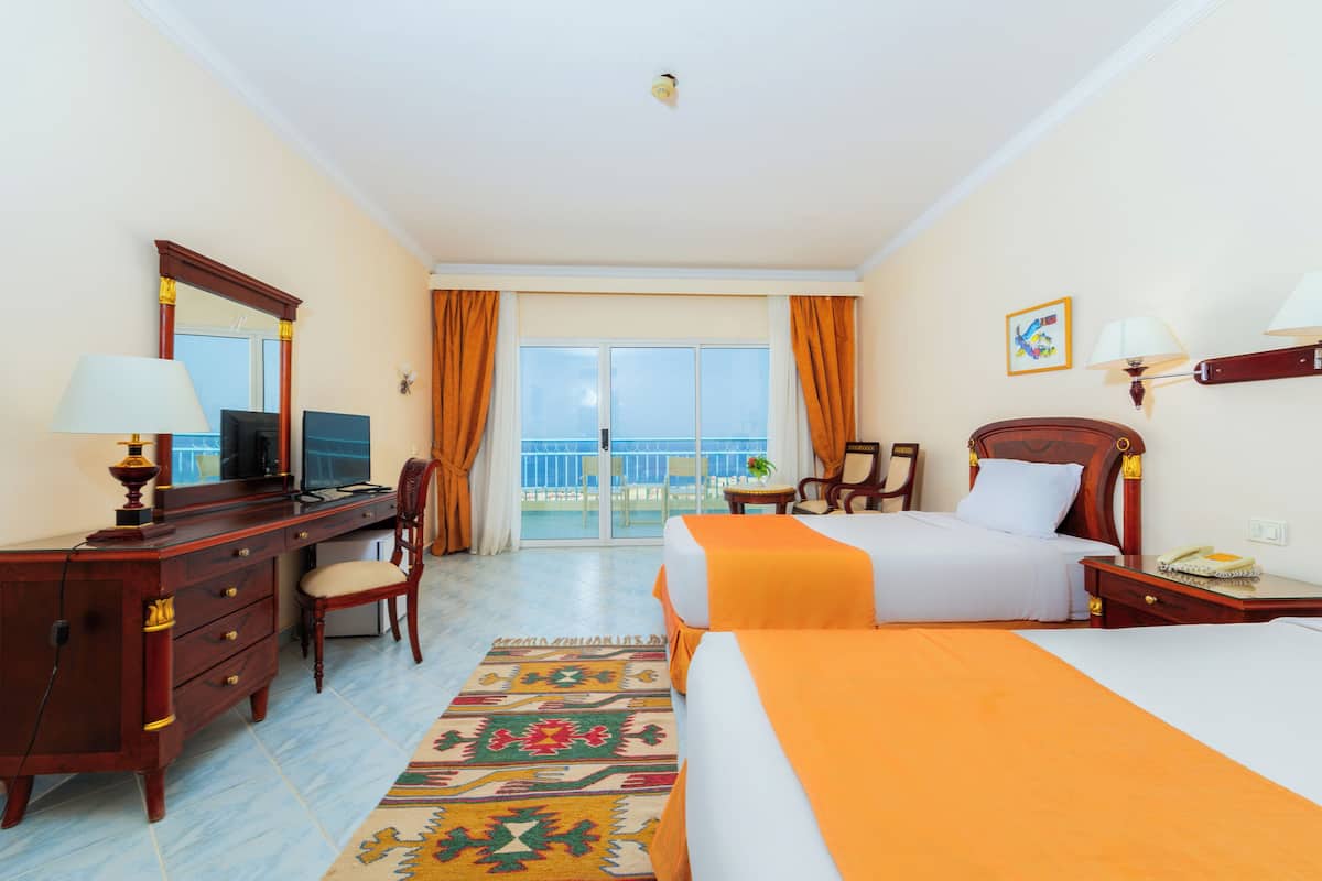 Een hotelkamer met een bed, bureau, stoel en uitzicht op zee.