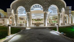 Entrada de hotel con una galería techada, columnas de piedra y asientos al aire libre.