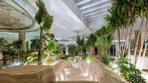 Un patio interior con fuente central, rodeado de plantas tropicales y paredes de piedra.