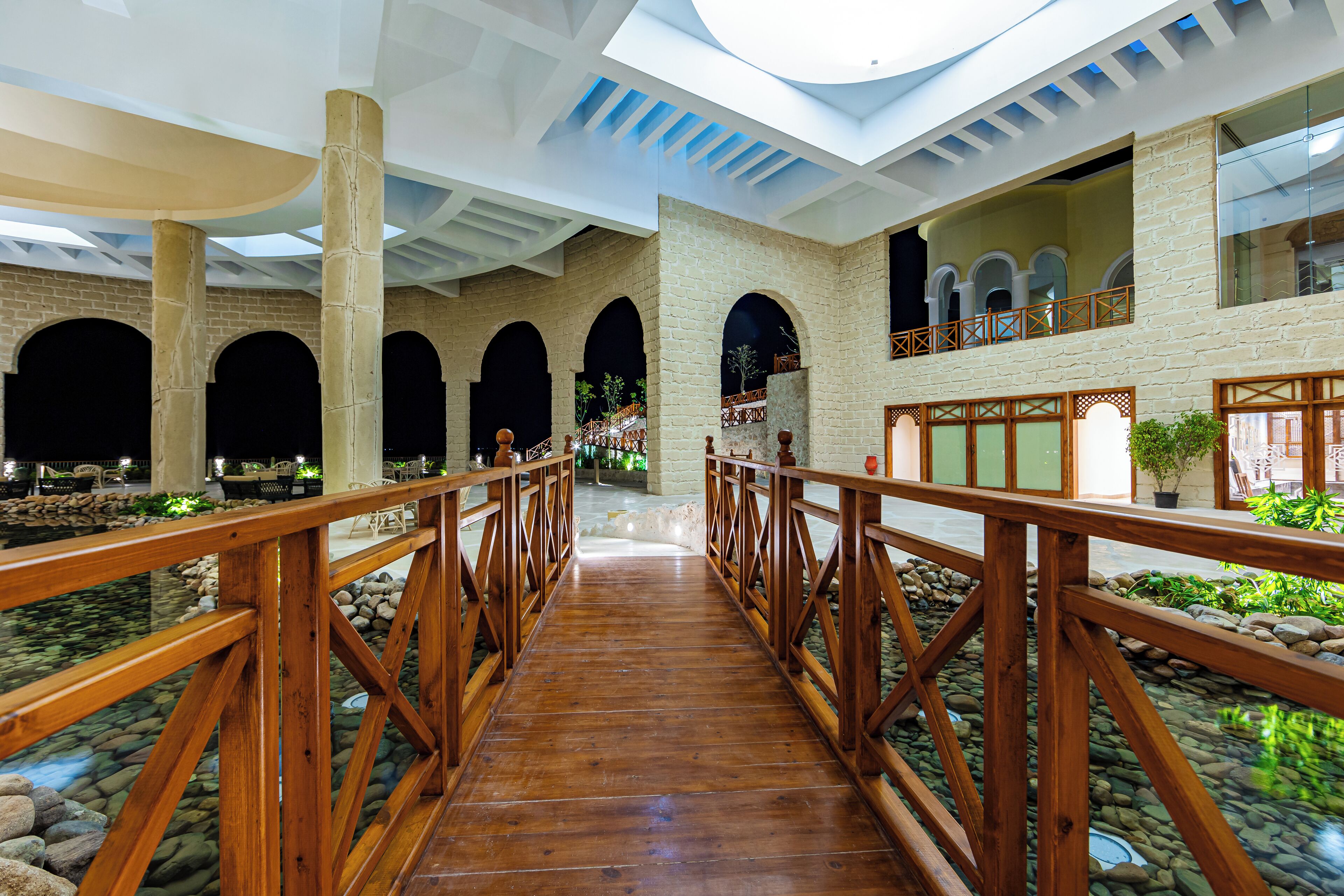A wooden bridge with railings in a hotel lobby with stone walls and arched doorways.