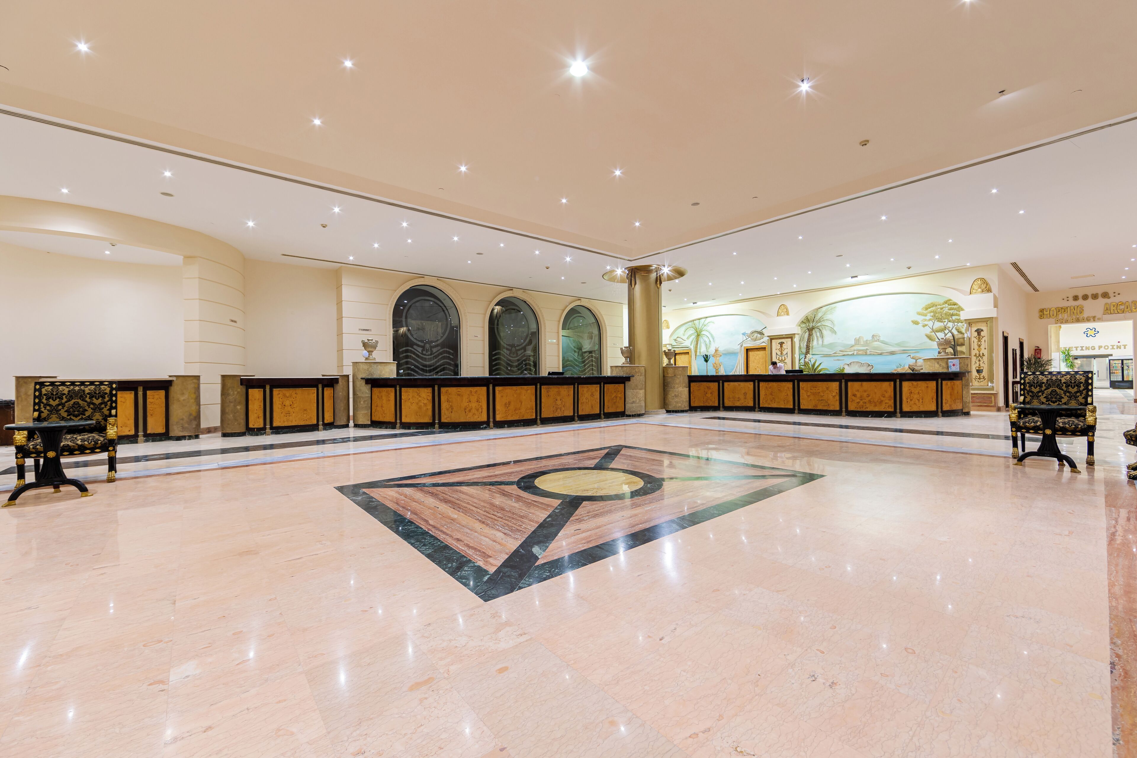 Um hall amplo com piso de mármore, balcão de recepção e um mural na parede.